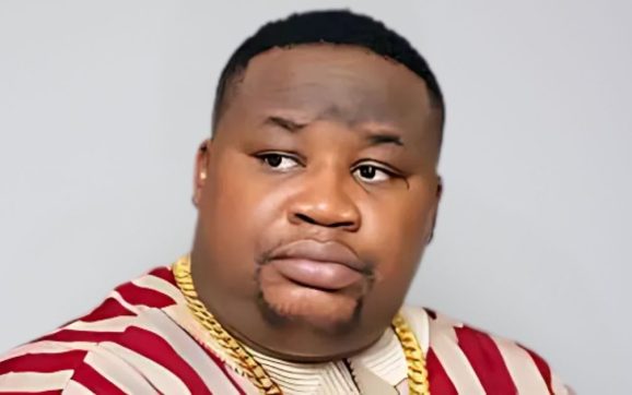 Cubana Chief Priest in a serious pose wearing a patterned shirt and gold chains, symbolizing his statement on naira spraying and EFCC crackdown.