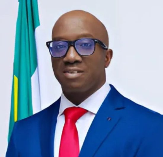 Governor Monday Okpebholo delivering a May Day speech outdoors at a stadium, standing behind a microphone in traditional attire.